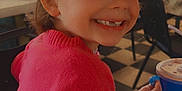 Lydia is registered to the contest to win money with this photo: child, girl, smiling, pink_sweater, headband, indoor, table, drink_cup, neon_effect, devil_horns, happy, portrait, seated, restaurant, checkered_floor, colorful_wall, hair_tied, cute, mischievous, casual_clothing