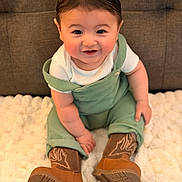 Jameson is registered to the contest to win money with this photo: baby, child, smiling, green_overalls, brown_boots, white_shirt, fluffy_blanket, indoor, cute, happy, sitting, portrait, face, skin, hair, footwear, one_person, infant, young_child, cozy