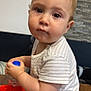 baby, toddler, child, water_bottle, striped_shirt, red_pants, indoor, wooden_table, curious, face, sitting, person, hand, clothing, couch, stone_wall, innocent, expression, young_child, casual_wear