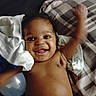 baby, child, infant, smiling, happy, waving, portrait, face, eyes, teeth, lying_down, bed, blanket, pillow, bedding, bottle, indoor, home, bare_chested, closeup