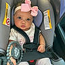 baby, car_seat, headband, pink_bow, teething_toy, curly_hair, clothing, infant, child, seatbelt, car_interior, cute, portrait, person, sitting, holding, toy, wide_eyes, sunlight, closeup