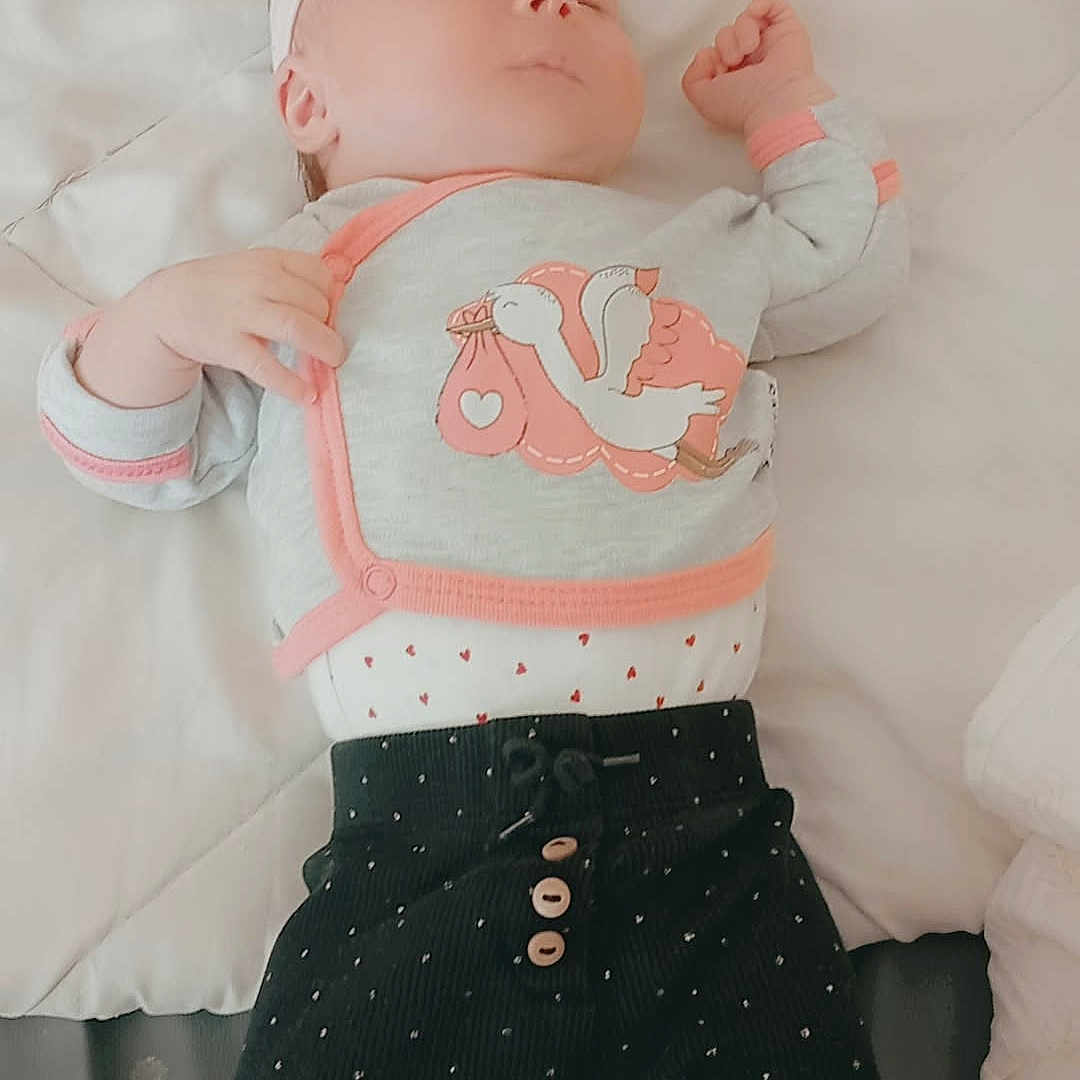 Georgina participe au concours pour gagner de l'argent avec cette photo : baby, sleeping, infant, clothing, headband, blanket, quilt, stork, patterned_pants, soft_toys, peaceful, indoors, cute, child, newborn, pink, black, orange, lying_down, cozy