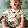 baby, infant, smiling, sitting, clothing, socks, bed, quilt, patterned_clothing, cute, happy, portrait, child, indoor, skin, face, person, young_child, tooth, expression
