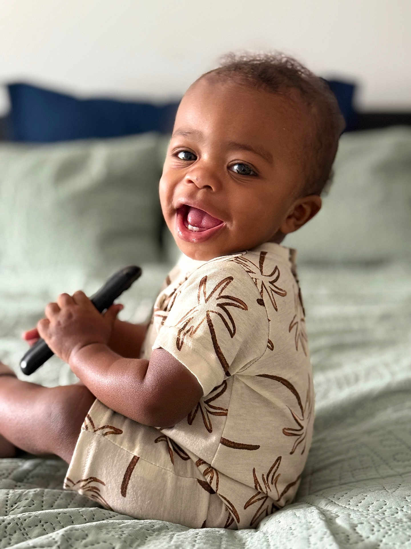 Zyaire is registered to the contest to win money with this photo: toddler, child, smiling, happy, sitting, bed, blanket, clothing, palm_tree_pattern, indoor, person, cute, portrait, baby, skin, hand, face, eyes, mouth, hair