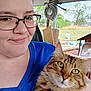 person, cat, glasses, smile, outdoor, tabby_cat, animal, pet, fur, hand, greenery, hose, wood, bucket, fan, chair, face, eye, nature, casual