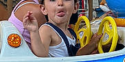 Lenzo participe au concours pour gagner de l'argent avec cette photo : child, adult, amusement_ride, blue, yellow, steering_wheel, cap, tongue_out, glasses, woman, lights, carousel, fun, playful, outdoor, person, face, hair, clothing, seat