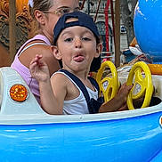 Lenzo participe au concours pour gagner de l'argent avec cette photo : child, amusement_ride, blue, cap, steering_wheel, woman, glasses, lights, carnival, playful, tongue_out, seat, fun, outdoor, summer, person, daytime, clothing, hair, face