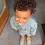 Lenzo participe au concours pour gagner de l'argent avec cette photo : toddler, child, curly_hair, pacifier, smiling, indoor, doorway, light_blue_sweatshirt, denim_shorts, sneakers, floor, tile_floor, standing, looking_up, happy, casual_clothing, young_child, person, footwear, playful