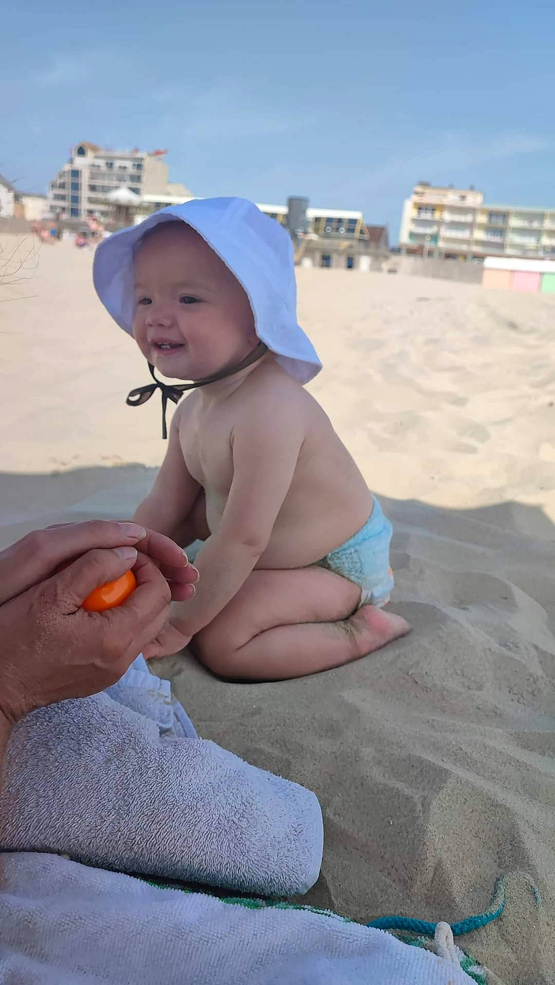 Ohana participe au concours pour gagner de l'argent avec cette photo : baby, beach, body_of_water, elbow, fun, happy, hat, headwear, human_leg, knee, landscape, leisure, natural_environment, people, people_on_beach, person, sand, sky, summer, sun_hat