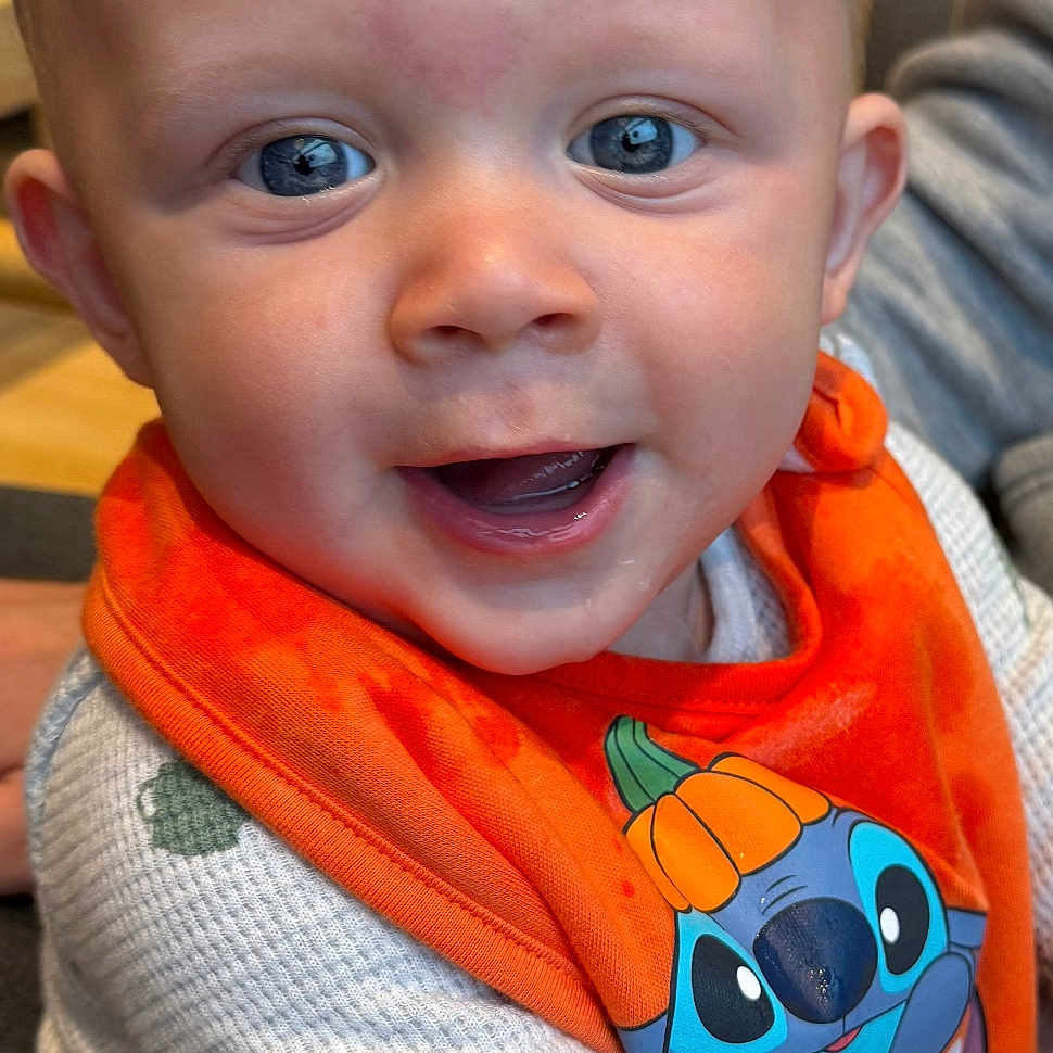 Finley is registered to the contest to win money with this photo: baby, blue_eyes, cartoon_character, child, closeup, clothing, cute, face, fun, happy, holiday, indoor, infant, orange_bib, person, portrait, pumpkin_hat, smiling, sweater, toddler