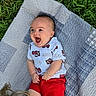 baby, infant, child, laughing, happy, outdoor, grass, quilt, blanket, clothing, red_shorts, white_shirt, patterned_shirt, person, head, smile, joy, playing, cute, sunlight