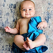 Levi is registered to the contest to win money with this photo: baby, infant, child, blue_cloth, bare_skin, lying_down, rug, floor, curious_expression, wide_eyes, chubby_cheeks, soft_texture, indoor, cute, portrait, human, small_hands, small_feet, skin, relaxed