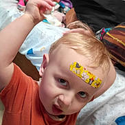 Waylon Chaos joined the competition — help win amazing prizes! bandage, bed, blanket, casual_clothing, child, curly_hair, cute, expression, face, forehead, furniture, home, indoor, orange_shirt, person, pillow, playful, portrait, toddler, young_child