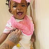 Bless'In joined the competition — help win amazing prizes! baby, child, smiling, laughing, portrait, pink_bow, headband, bib, striped_shirt, white_clothing, baby_outfit, curly_hair, indoors, wall, closeup, happy, sitting, adult_hand, tattoo, photography