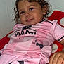 toddler, child, curly_hair, pink_clothing, soccer_jersey, sport_outfit, drool, blanket, red_blanket, white_blanket, relaxed, smile, indoor, portrait, person, hand, face, eyes, couch, casual