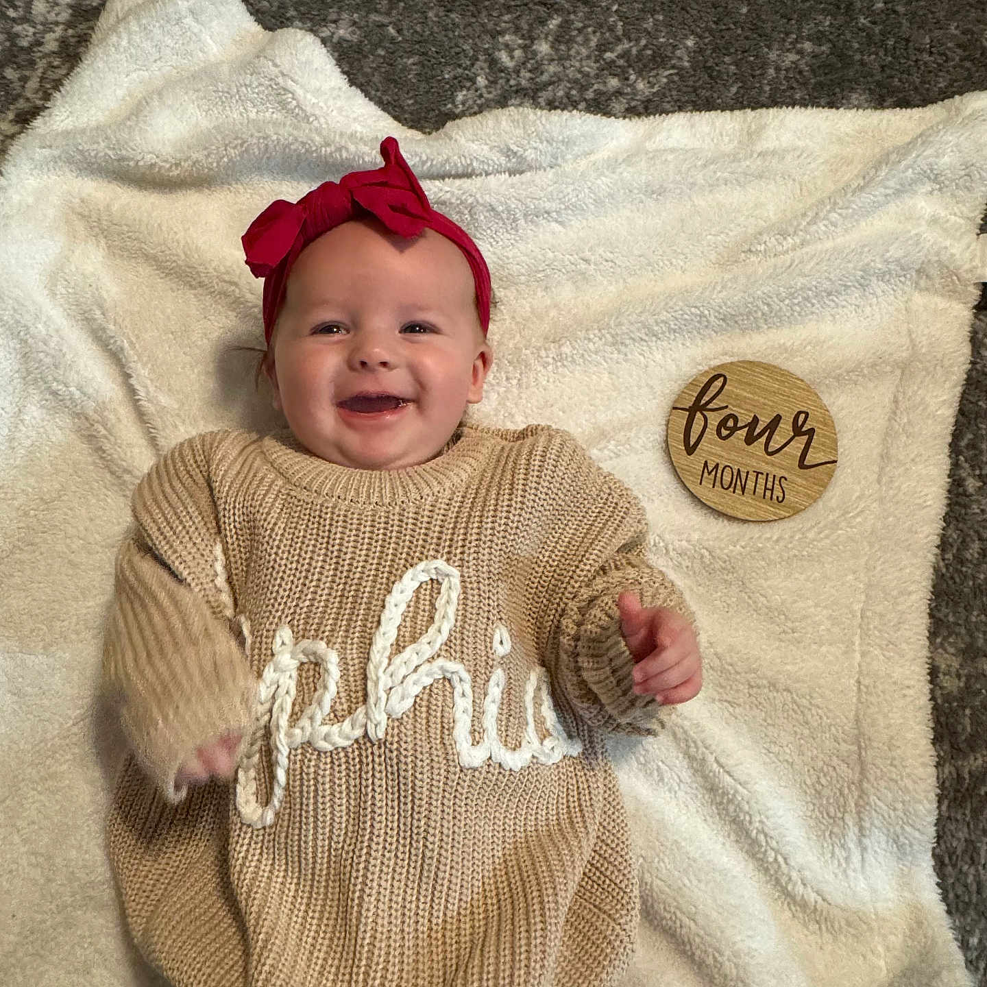 Sophia joined the competition — help win amazing prizes! baby, blanket, child, cozy, cute, four_months, happy, headband, indoors, infant, knitwear, lying_down, person, portrait, smiling, soft_texture, sweater, wearing_clothes, wooden_plaque, young_child