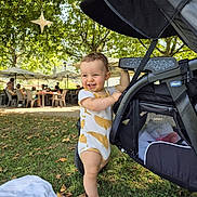 Valentin participe au concours pour gagner de l'argent avec cette photo : toddler, child, smiling, barefoot, stroller, grass, outdoor, tree, leaf, umbrella, people, sunlight, park, daytime, happy, clothing, nature, bench, picnic, baby