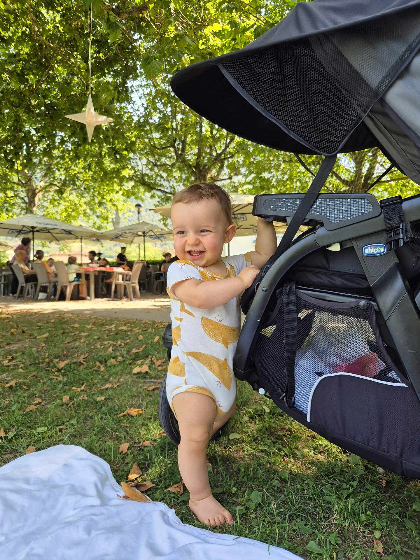 Valentin participe au concours pour gagner de l'argent avec cette photo : toddler, child, smiling, barefoot, stroller, grass, outdoor, tree, leaf, umbrella, people, sunlight, park, daytime, happy, clothing, nature, bench, picnic, baby