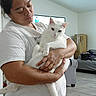 cardboard_box, casual_clothing, cat, comfort, couch, domestic_animal, floor, furniture, holding, home, human, indoor, living_room, person, pet, relaxed, short_sleeve, television, white_cat, wood_floor