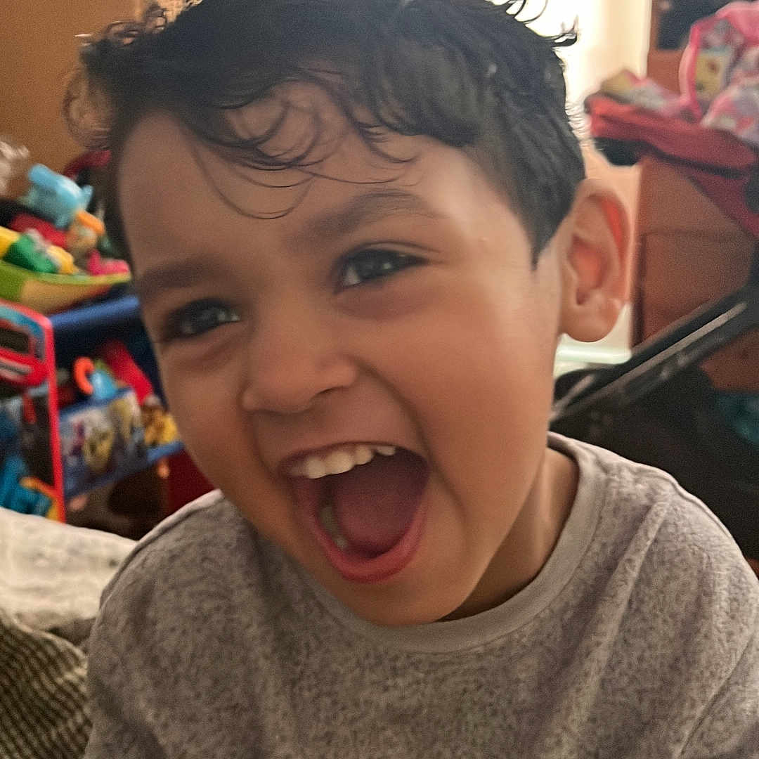 Noah Silva is registered to the contest to win money with this photo: child, childhood, closeup, cute, expression, face, fun, furniture, gray_sweater, happy, home, indoor, laughing, person, playful, portrait, smiling, toy, wet_hair, young