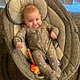 baby, infant, baby_rocker, onesie, smiling, toy, carpet, indoor, face, person, child, clothing, seat, comfort, home, vertical_blinds, pattern, footed_pajamas, happy, young_child