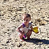 child, toddler, beach, sand, outdoor, summer, bucket, shovel, toy, crouching, sitting, portrait, face, hair, clothing, barefoot, sunlight, shoreline, play, sandcastle