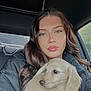 woman, puppy, dog, car_interior, portrait, long_hair, brown_hair, blue_eyes, jacket, black_jacket, pet, holding, indoor, natural_light, cute, companion, young_adult, casual, soft_light, close_up