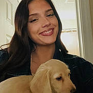 Melania is registered to the contest to win money with this photo: woman, smile, puppy, dog, golden_retriever, indoor, door, curtain, long_hair, jacket, holding, pet, happy, face, portrait, young_adult, casual, warm_lighting, human, animal