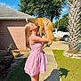 Gingy is registered to the contest to win money with this photo: woman, cat, pink_dress, outdoor, sunny, sidewalk, brick_house, palm_tree, white_truck, green_grass, tree, daylight, kiss, holding, shadow, pet, happy, casual, nature, portrait