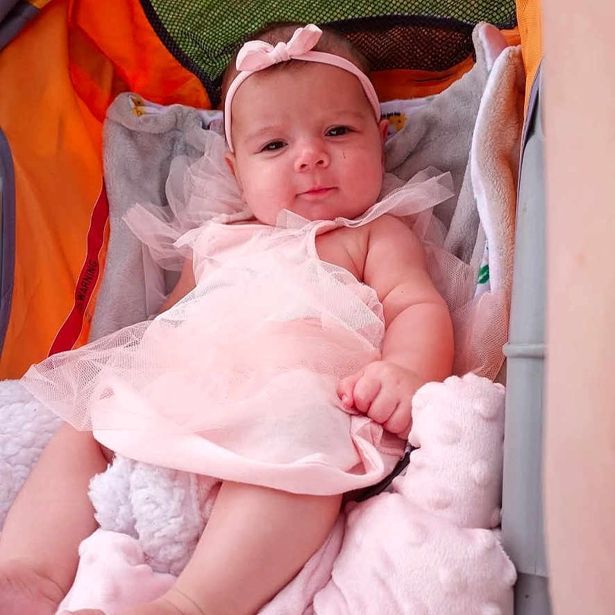 River is registered to the contest to win money with this photo: baby, baby_feet, baby_hand, blanket, child, cute, fabric, gray, headband, indoors, infant, mesh, orange, pink_dress, portrait, relaxed, smiling, soft_toys, stroller, tulle