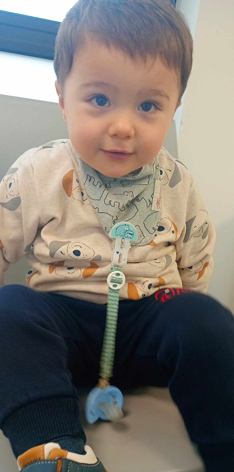 Leo participe au concours pour gagner de l'argent avec cette photo : child, toddler, baby, pacifier, bib, dog_print, shirt, pants, shoe, blue_eyes, sitting, indoor, window, seat, cute, portrait, smiling, accessory, pacifier_clip, clothing