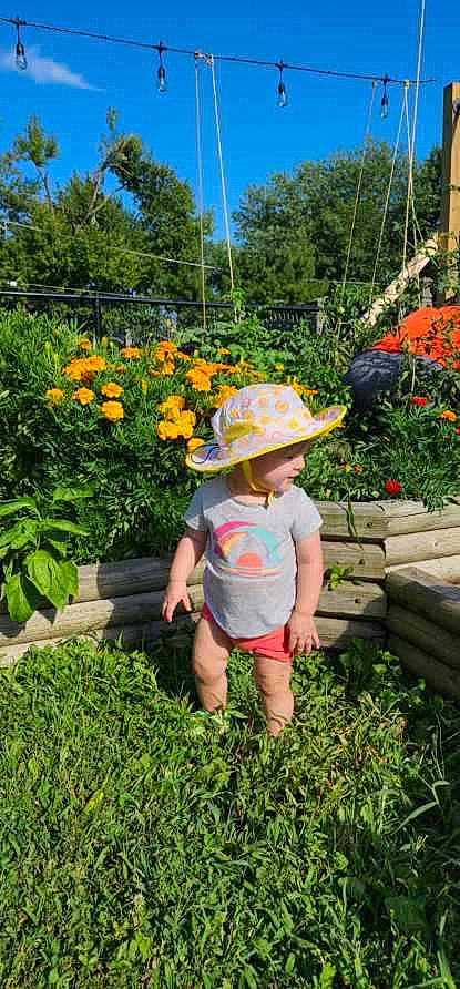 Caroline is registered to the contest to win money with this photo: baby, flower, fun, garden, grass, groundcover, happy, hat, headwear, landscape, leaf, leisure, people_in_nature, person, plant, shorts, shrub, sky, summer, sun_hat