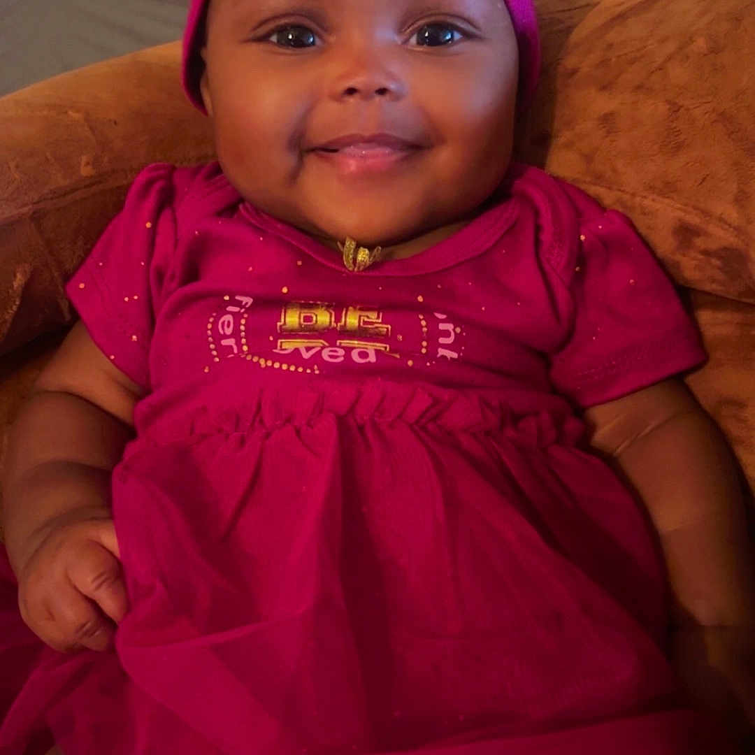 Ivory is registered to the contest to win money with this photo: baby, child, smiling, pink_dress, headband, sitting, couch, indoors, happy, cute, portrait, infant, person, clothing, fabric, skin, face, headwear, comfort, warmth