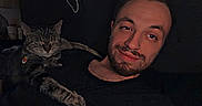 Jade is registered to the contest to win money with this photo: beard, casual_clothing, cat, closeup, comfort, companion, couch, dark_background, domestic, evening, feline, friendship, indoor, man, pet, portrait, relaxed, resting, sleepy, smile