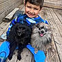 animal, black_dog, blue_clothing, boots, boy, child, cute, dog, face, fluffy_dog, fur, gray_dog, happy, nature, outdoor, pet, sitting, small_dog, smile, wooden_deck