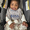 baby, infant, smiling, bib, car_seat, pajamas, clothing, face, hand, happy, child, cute, indoors, seat, portrait, person, young, sitting, fabric, text