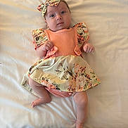 Matilda is registered to the contest to win money with this photo: baby, infant, child, lying_down, floral_dress, headband, bow, cute, skin, face, hands, legs, blanket, soft_light, indoors, portrait, looking_at_camera, expression, clothing, comfort