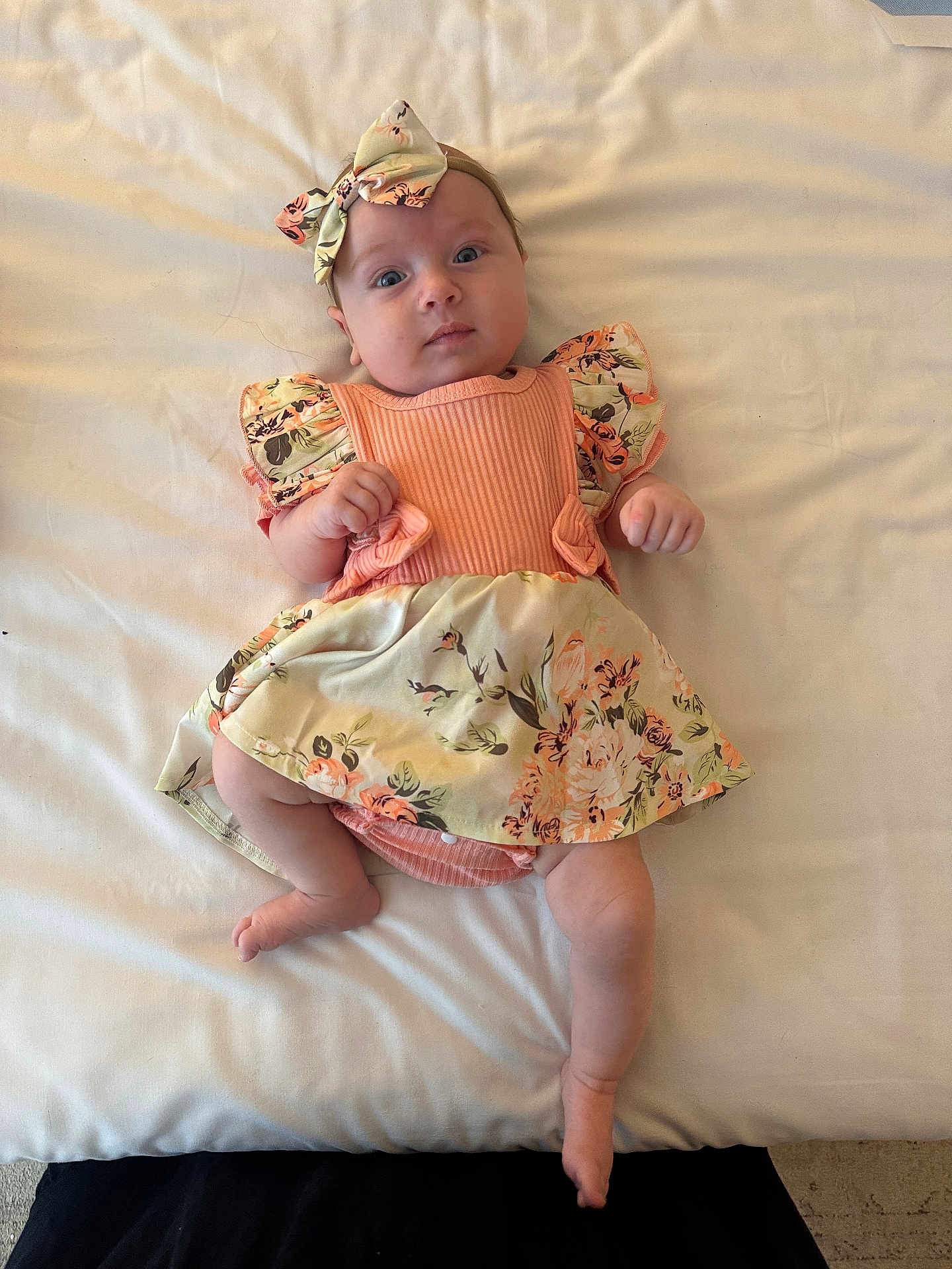 Matilda is registered to the contest to win money with this photo: baby, infant, child, lying_down, floral_dress, headband, bow, cute, skin, face, hands, legs, blanket, soft_light, indoors, portrait, looking_at_camera, expression, clothing, comfort