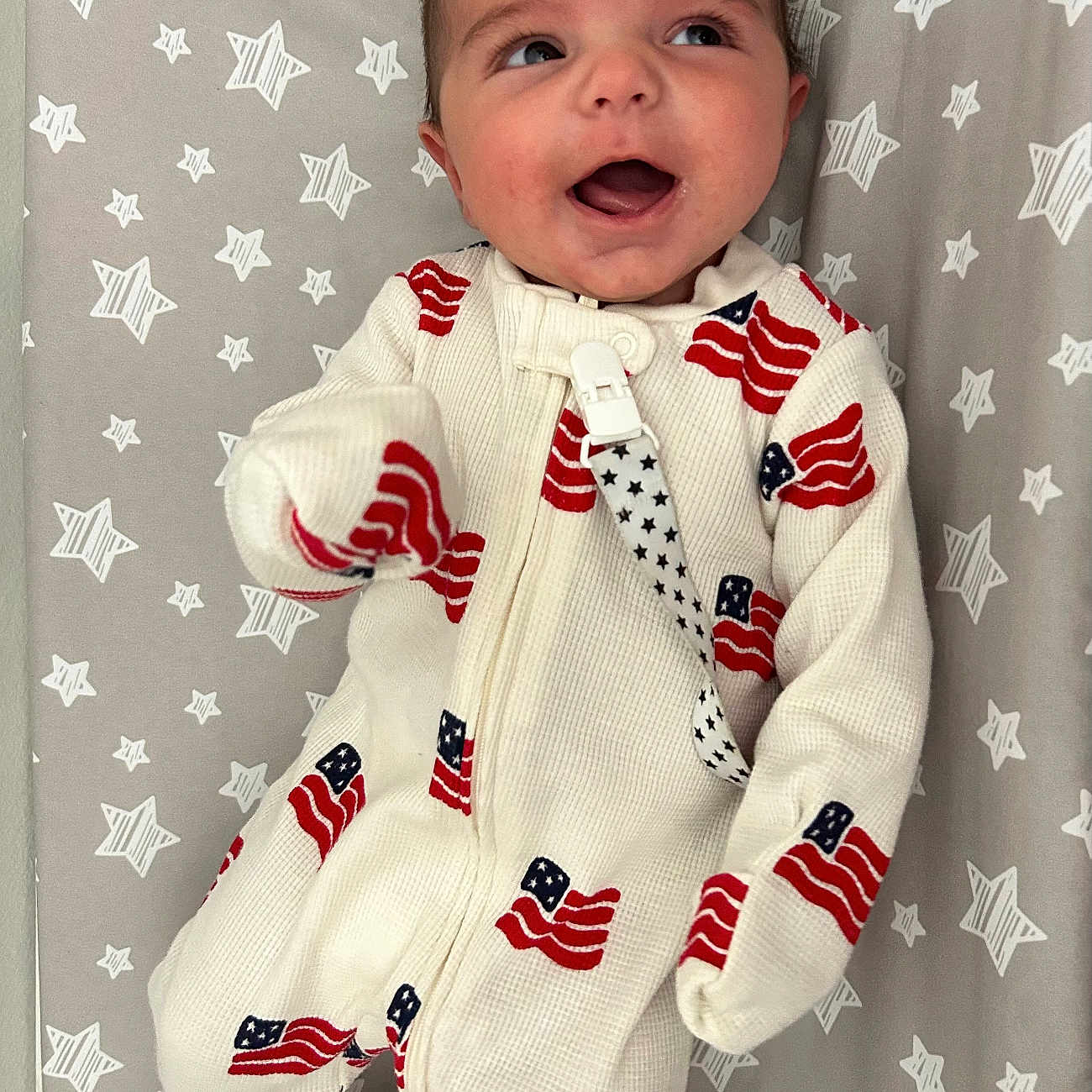 Kota joined the competition — help win amazing prizes! baby, infant, onesie, american_flag, stars_pattern, blanket, smiling, happy, lying_down, cute, child, face, head, clothing, fabric, pattern, indoors, young_child, person, apparel