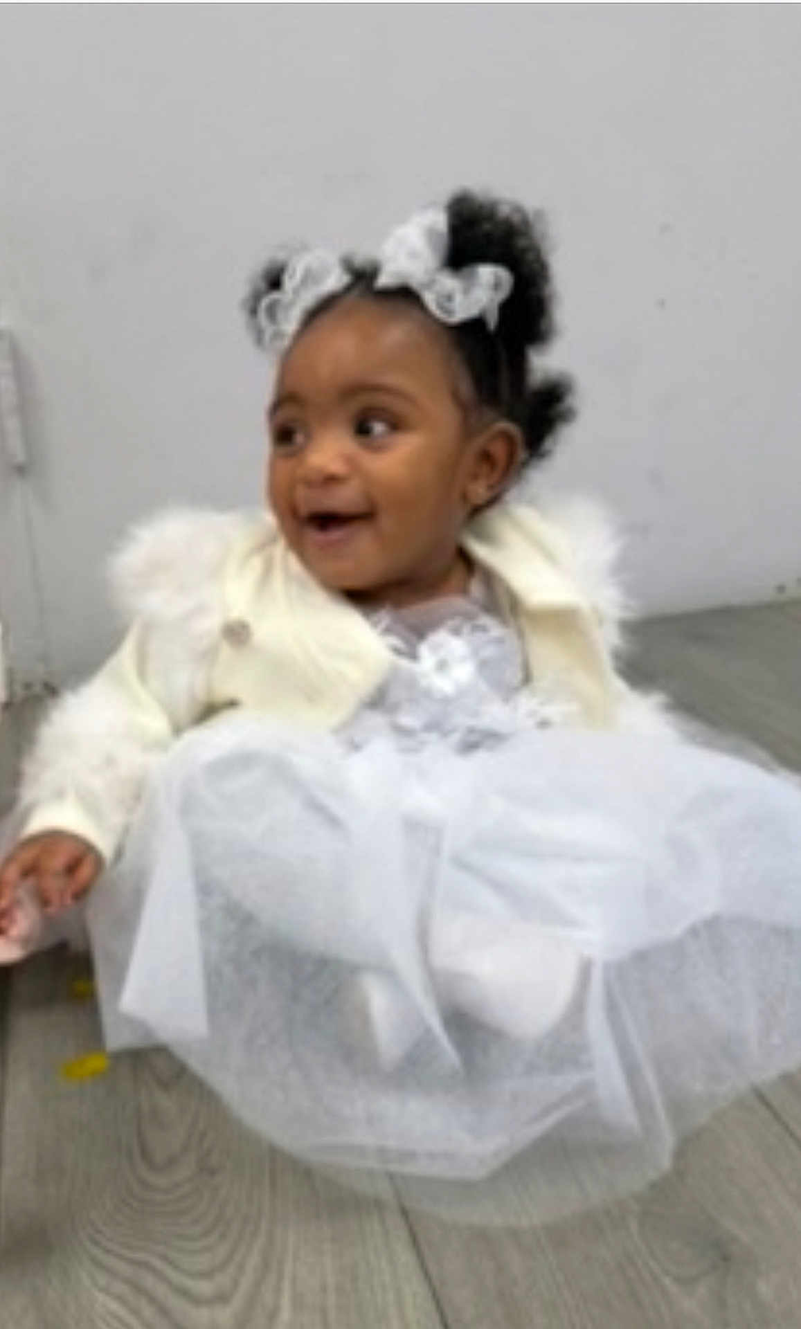 Jaliyah joined the competition — help win amazing prizes! child, girl, baby, dress, white_dress, jacket, lace_bows, curly_hair, smiling, sitting, floor, wooden_floor, indoors, happy, cute, portrait, person, fashion, toddler, young_child