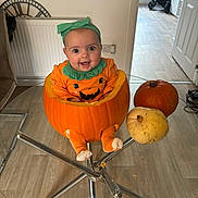 Cali-Rose joined the competition — help win amazing prizes! baby, pumpkin, halloween, costume, table, glass_table, indoor, child, smiling, orange, headband, legs, floor, chair, radiator, door, baby_clothing, happy, festive, decor
