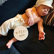Zayden is registered to the contest to win money with this photo: baby, sleeping, infant, one_month, suspenders, cap, couch, pillow, wooden_sign, milestone, peaceful, cute, clothing, resting, hand, foot, portrait, indoors, child, person