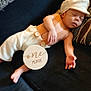 baby, sleeping, infant, one_month, suspenders, cap, couch, pillow, wooden_sign, milestone, peaceful, cute, clothing, resting, hand, foot, portrait, indoors, child, person