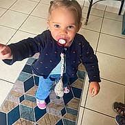 Jélyana a rejoint le concours — aidez-le/la à gagner de superbes lots ! toddler, child, pacifier, indoor, rug, tile_floor, sweater, jeans, shoes, person, cute, curious, standing, home, flooring, furniture, clothing, accessory, hair_tie, toy