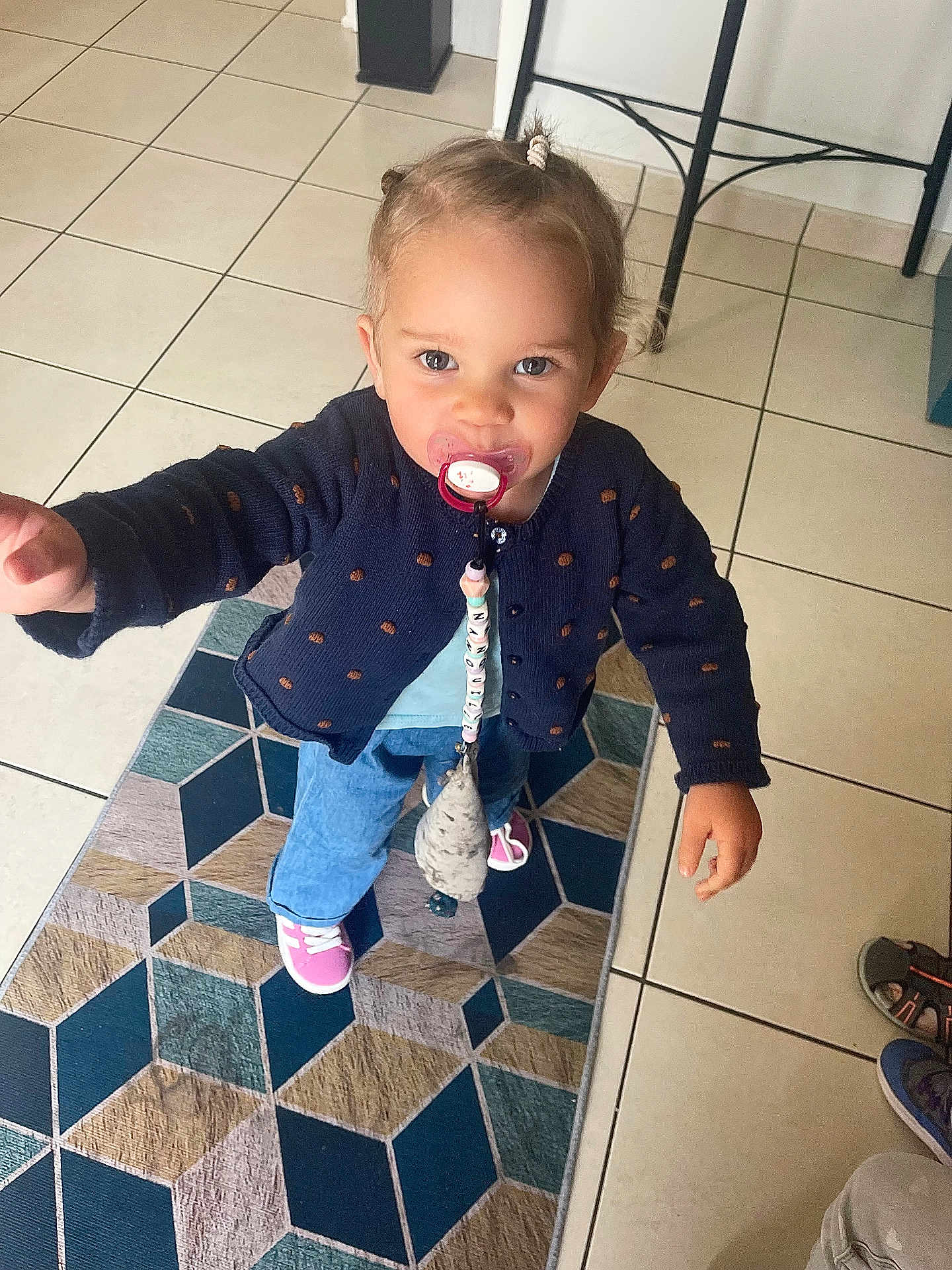 Jélyana a rejoint le concours — aidez-le/la à gagner de superbes lots ! toddler, child, pacifier, indoor, rug, tile_floor, sweater, jeans, shoes, person, cute, curious, standing, home, flooring, furniture, clothing, accessory, hair_tie, toy