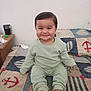 baby, bed, child, clothing, comfort, cute, face, foot, green_outfit, hair, happy, home, indoor, infant, pajamas, person, quilt, sitting, smile, toddler