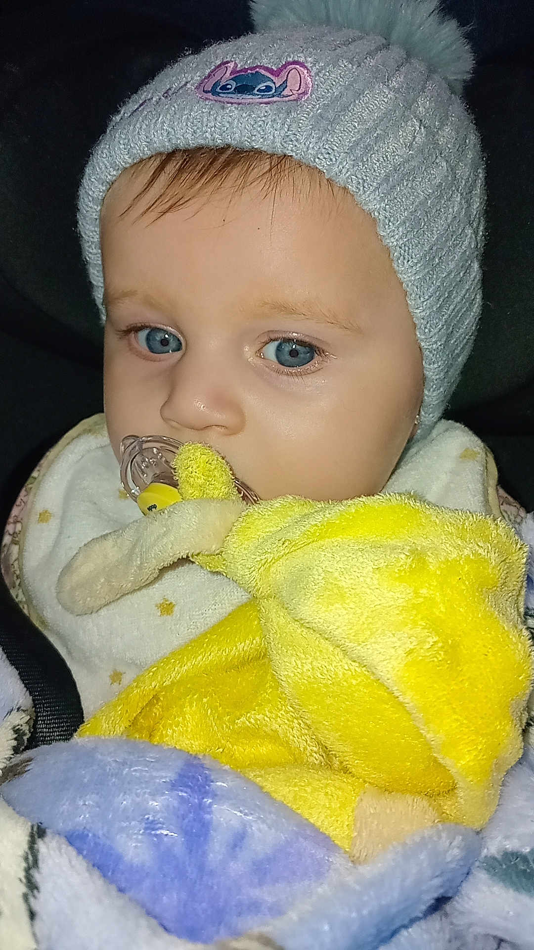 Christine Santiago participe au concours pour gagner de l'argent avec cette photo : baby, child, pacifier, hat, knitted_hat, blanket, plush_toy, blue_eyes, close_up, cozy, warm, indoor, portrait, soft_texture, infant, cute, sleepy, yellow, clothing, comfort