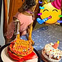 dog, birthday, cake, party_hat, pink_clothing, crown, table, celebration, decorations, balloon, ribbon, sprinkles, indoor, pet, festive, costume, collar, wooden_wall, emoji_sticker, first_birthday