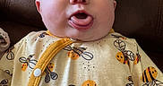 Guinevere joined the competition — help win amazing prizes! baby, bee_pattern, brown, buttoned, child, clothing, couch, cute, expression, face, funny_face, indoors, infant, person, plush, portrait, sitting, smiling_bees, tongue, yellow_onesie