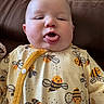 baby, bee_pattern, brown, buttoned, child, clothing, couch, cute, expression, face, funny_face, indoors, infant, person, plush, portrait, sitting, smiling_bees, tongue, yellow_onesie